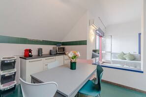 Una cocina compacta con comedor, microondas, tetera y un asiento junto a la ventana con cojines.