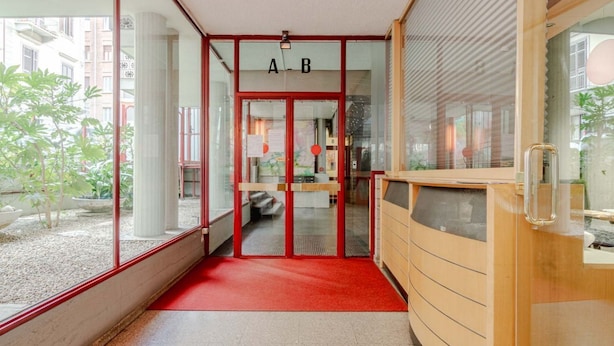 Entrada de hotel con alfombra roja, puertas de cristal y un letrero que dice 'A-B'.