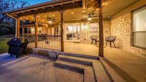 A covered outdoor patio with a grill, stone walls, and a view of the interior.