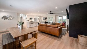 A spacious living area with a wooden dining table, a leather sofa, and a kitchen in the background.