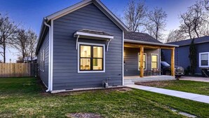Une maison moderne à deux étages, avec une façade de couleur gris foncé, un porche abrité et un garage apparent.