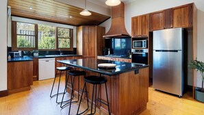 Une cuisine moderne avec des meubles en bois, un réfrigérateur en acier inoxydable, un îlot central doté de tabourets et une grande fenêtre qui laisse entrer la lumière naturelle.