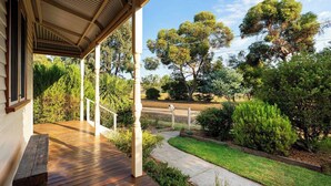 Une terrasse en bois avec un porche abrité, entourée d’un jardin bien entretenu et d’arbres.