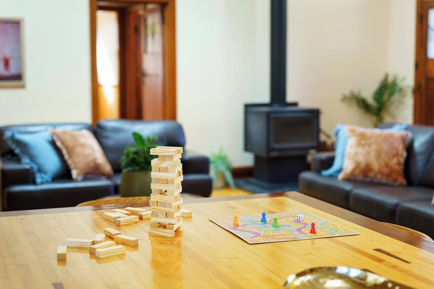 Un salon avec une table basse en bois, une pile de jeux Jenga et un jeu de société. On aperçoit un canapé et un téléviseur au fond de la pièce.