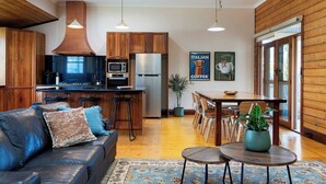 Une cuisine moderne avec des meubles en bois, un réfrigérateur en acier inoxydable et un coin bar. On y trouve une table à manger avec des chaises et une plante en pot.