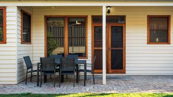 A covered patio with a table and chairs, a wooden fence, and a house with white siding and brown trim.