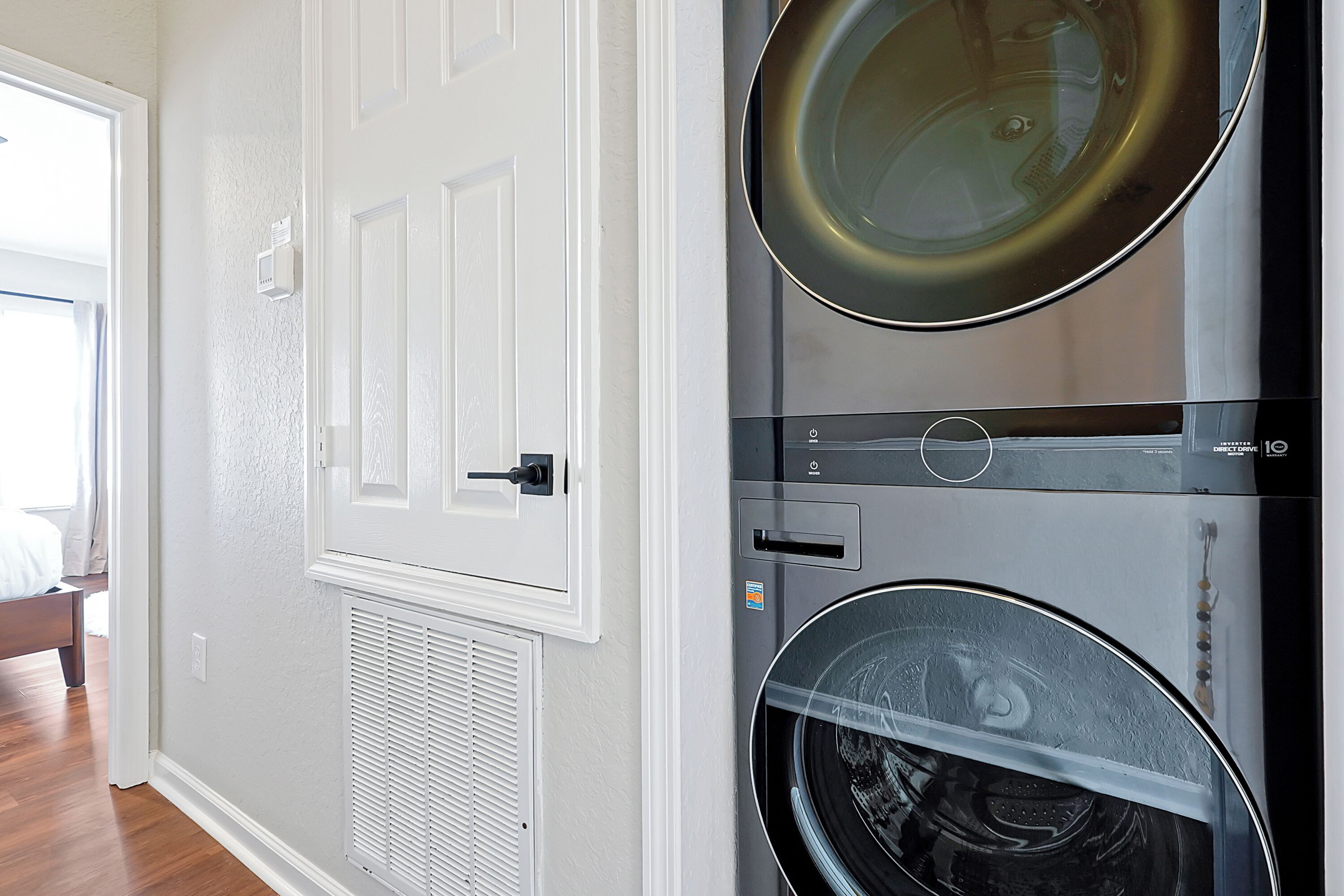 A laundry room with two stacked washing machines, a white door, and a vent.