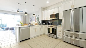A modern kitchen with white cabinets, stainless steel appliances, and pendant lighting.