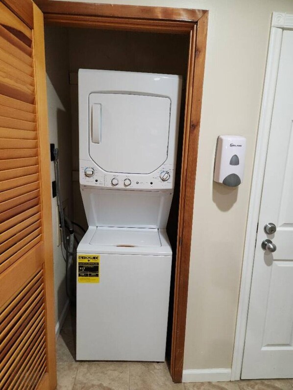 Una lavadora y secadora compactas con una etiqueta visible de ENERGYGUIDE, ubicadas en un espacio reducido con un marco de puerta de madera y una puerta blanca.