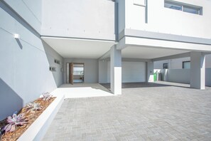 A modern building with a covered outdoor area, a paved walkway, and a small garden with plants. - The View Langebaan with Heated Pool (Langebaan)
