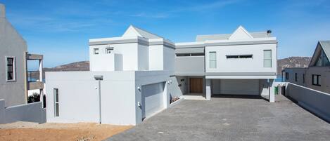 A modern residential building with a garage, a driveway, and a clear blue sky.