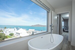 A modern bathroom with a large bathtub, a view of the ocean, and a glimpse of the interior. - The View Langebaan with Heated Pool (Langebaan)