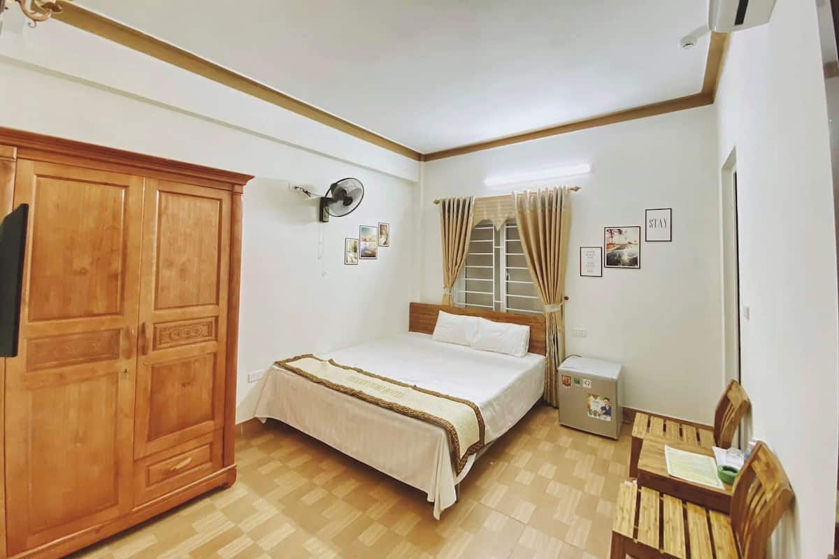 Ein Schlafzimmer mit Bett, Holzschrank, Nachttisch und kleinem Schreibtisch mit Stuhl.