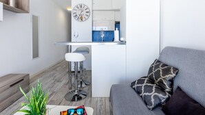 Un espace de vie compact comprenant un coin cuisine, un coin repas et un canapé agrémenté de coussins à motifs.
