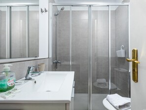 Une salle de bain moderne avec une douche à parois de verre, un lavabo blanc doté d’un distributeur de savon et un porte-serviettes.