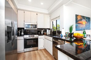 A modern kitchen with stainless steel appliances, white cabinetry, and a large island with a bowl of fruit.