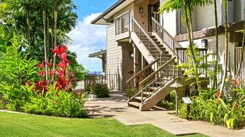 A two-story house with a staircase leading to the upper floor, surrounded by lush tropical plants and a well-maintained lawn.