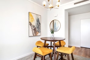 A dining area with a round table, four yellow chairs, a potted plant, and two wall-mounted artworks.