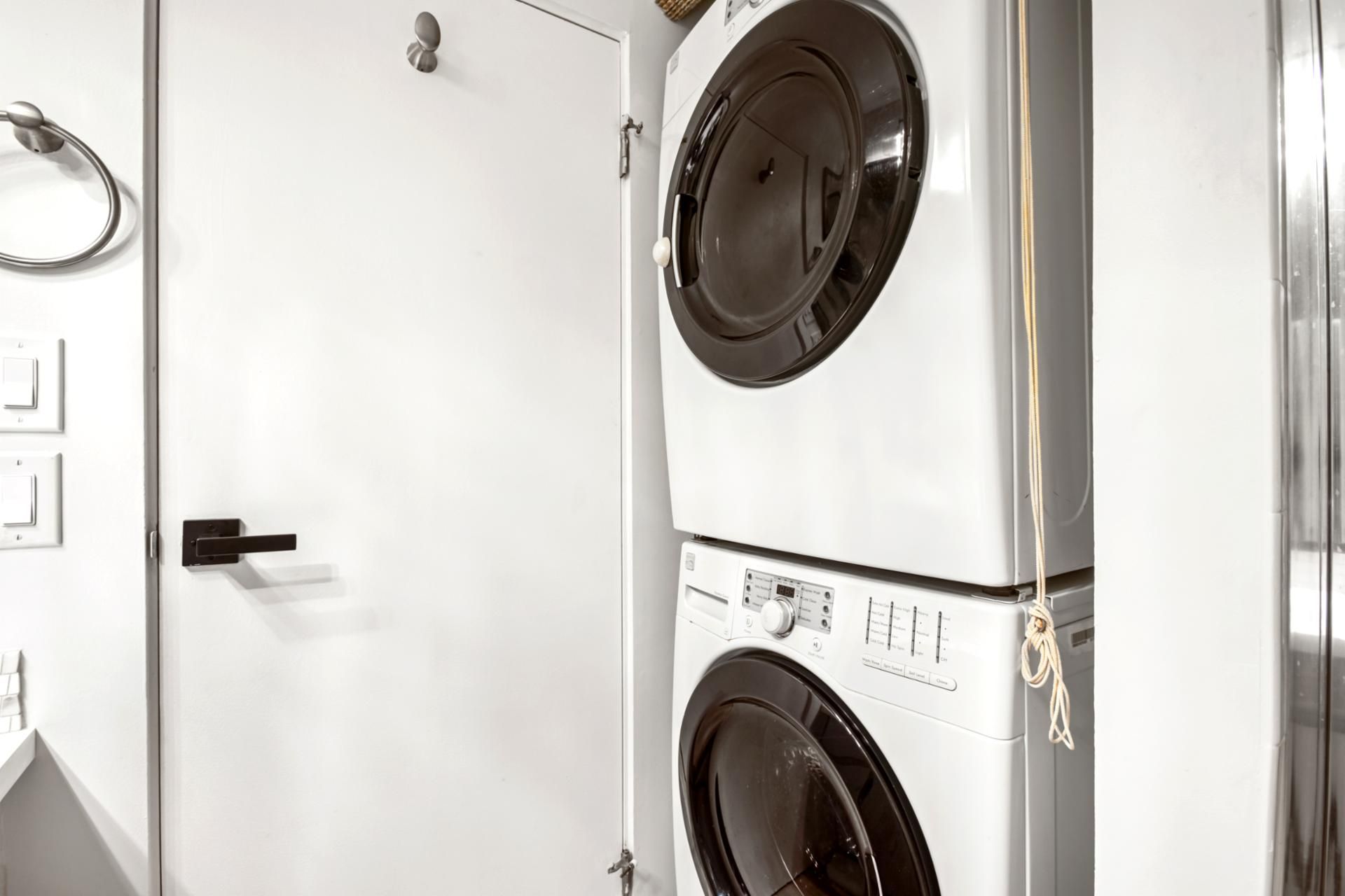 A laundry room with two stacked front-loading washing machines, a door with a handle, and a towel rack.