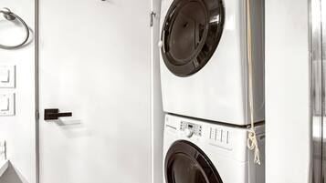 A laundry room with two stacked front-loading washing machines, a door with a handle, and a towel rack.