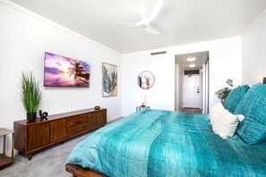 Un dormitorio con una cama, ventilador de techo, televisor, armario y una puerta que da a otra habitación.
