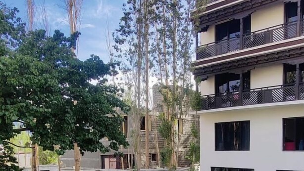 A courtyard with a well-maintained lawn, outdoor seating, and a multi-story building with balconies. - Hotel Choskor (Leh)