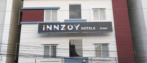 A hotel with a sign for 'INNZOY HOTELS' and a shop named 'DESIGNA' offering tea, snacks, and milkshakes.