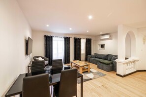A modern living room with a dining area, a sofa, a TV, and an air conditioning unit. - Appartement Confort & Serenite 2bdr/4p (Cannes)