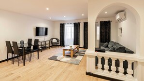 A modern living room with a dining area, a flat-screen TV mounted on the wall, and a sofa in a semi-enclosed space with an arched doorway. - Appartement Confort & Serenite 2bdr/4p (Cannes)