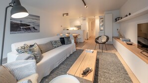 A modern living room with a sofa, coffee table, and a dining area in the background. - Apartment Near Albert Beach With Terrace (Knokke-Heist)