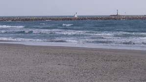 A beach with waves, a rocky breakwater, and two lighthouses in the distance.