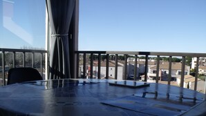 A round table with a tablecloth, a chair, and a view of buildings through a balcony railing.
