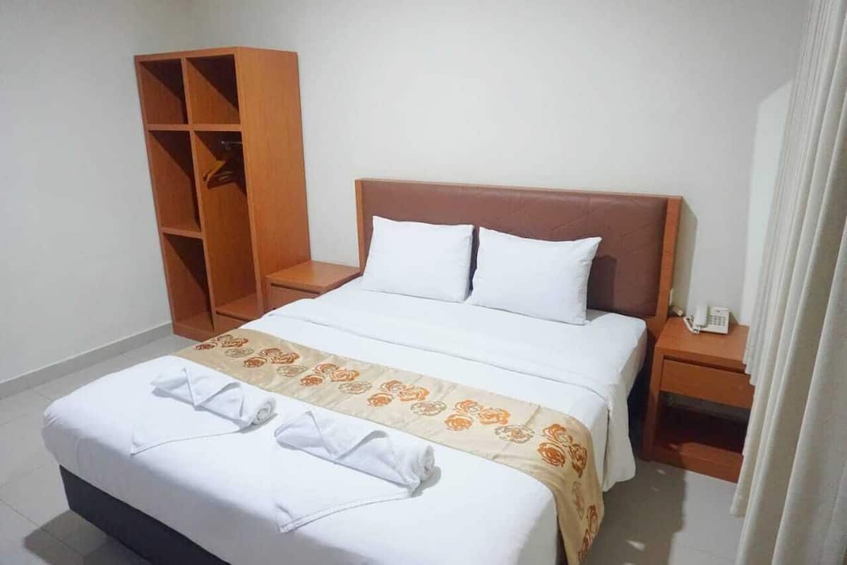 Une chambre d’hôtel avec un lit, une armoire en bois, une table de chevet avec un téléphone et un rideau.