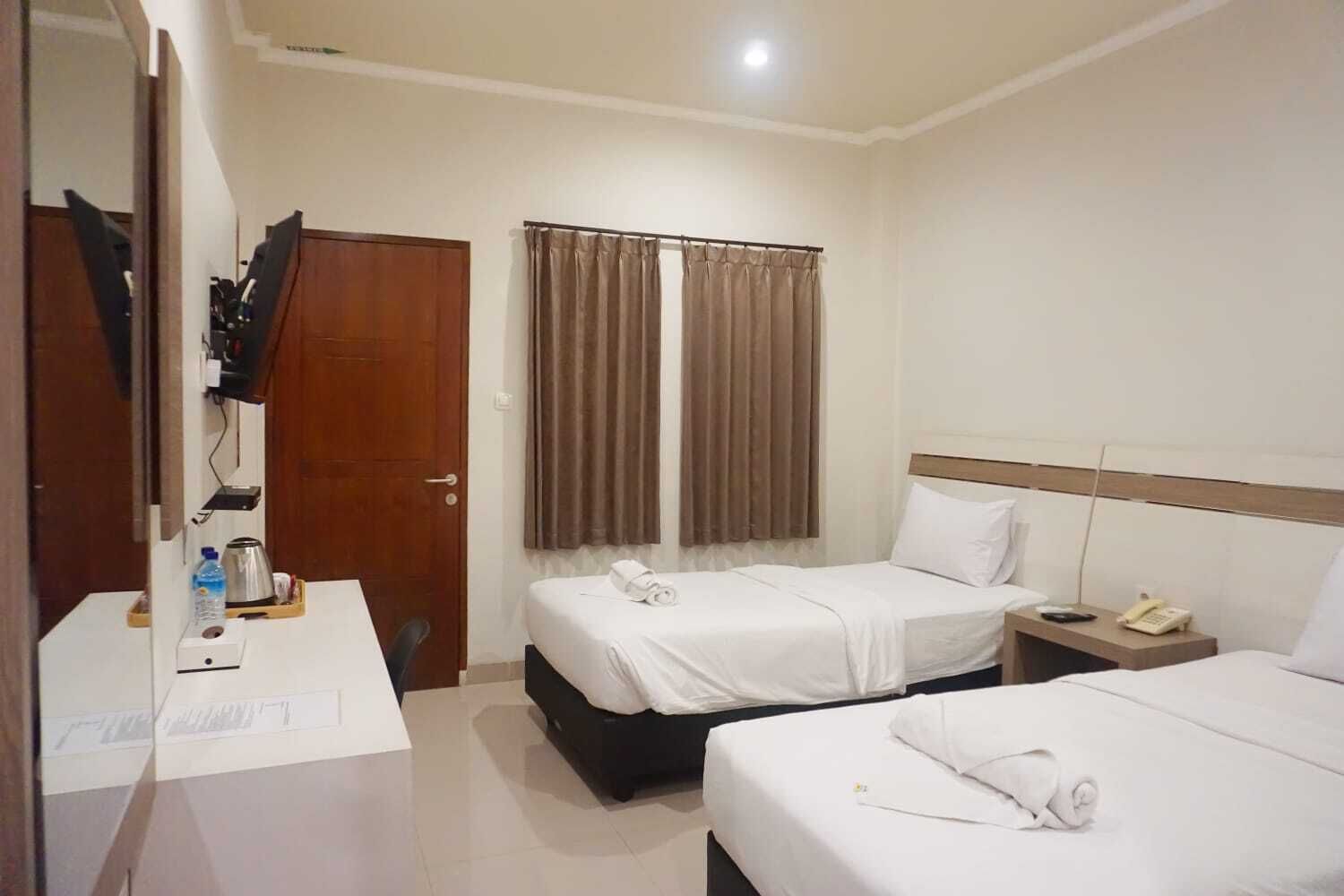 A hotel room with two beds, a desk with a telephone, and a mirror.
