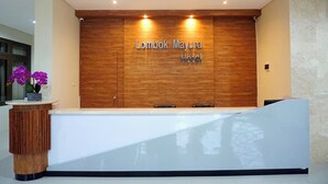 Un comptoir d’accueil avec un panneau en bois et l’inscription « Lombok Mayura Hotel » affichée au-dessus.