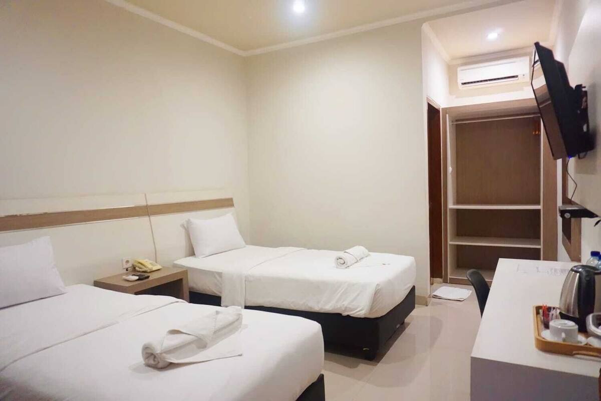 Une chambre d’hôtel avec deux lits, un bureau avec une chaise, un téléviseur fixé au mur et une armoire.
