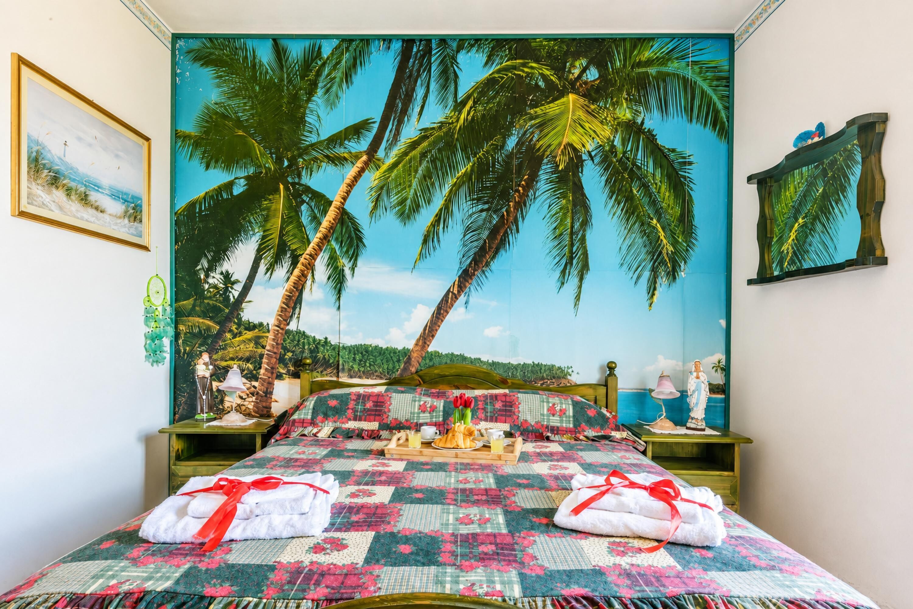 A bed with a tropical-themed headboard, a bedside table with a lamp, and a wall mural of palm trees.