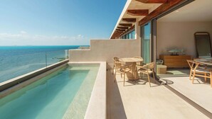 Un balcón moderno al aire libre con piscina, mobiliario de madera y vista al océano.