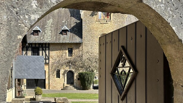 Un edificio de piedra con una entrada de arco tradicional, un portón de madera y un pequeño ventanal con diseño triangular.