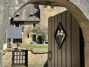 A stone building with a traditional arched entrance, a wooden gate, and a small window with a triangular design.