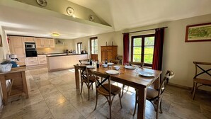 A spacious kitchen with a dining area, featuring a wooden table set for four, a large window with curtains, and a view of greenery outside. - Charming gite not far from the Orval Abbey (Orval)