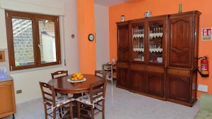Ein Essbereich mit Holztisch, Stühlen und einer Obstschale. An der Wand befindet sich ein großer Holzschrank und eine Uhr.