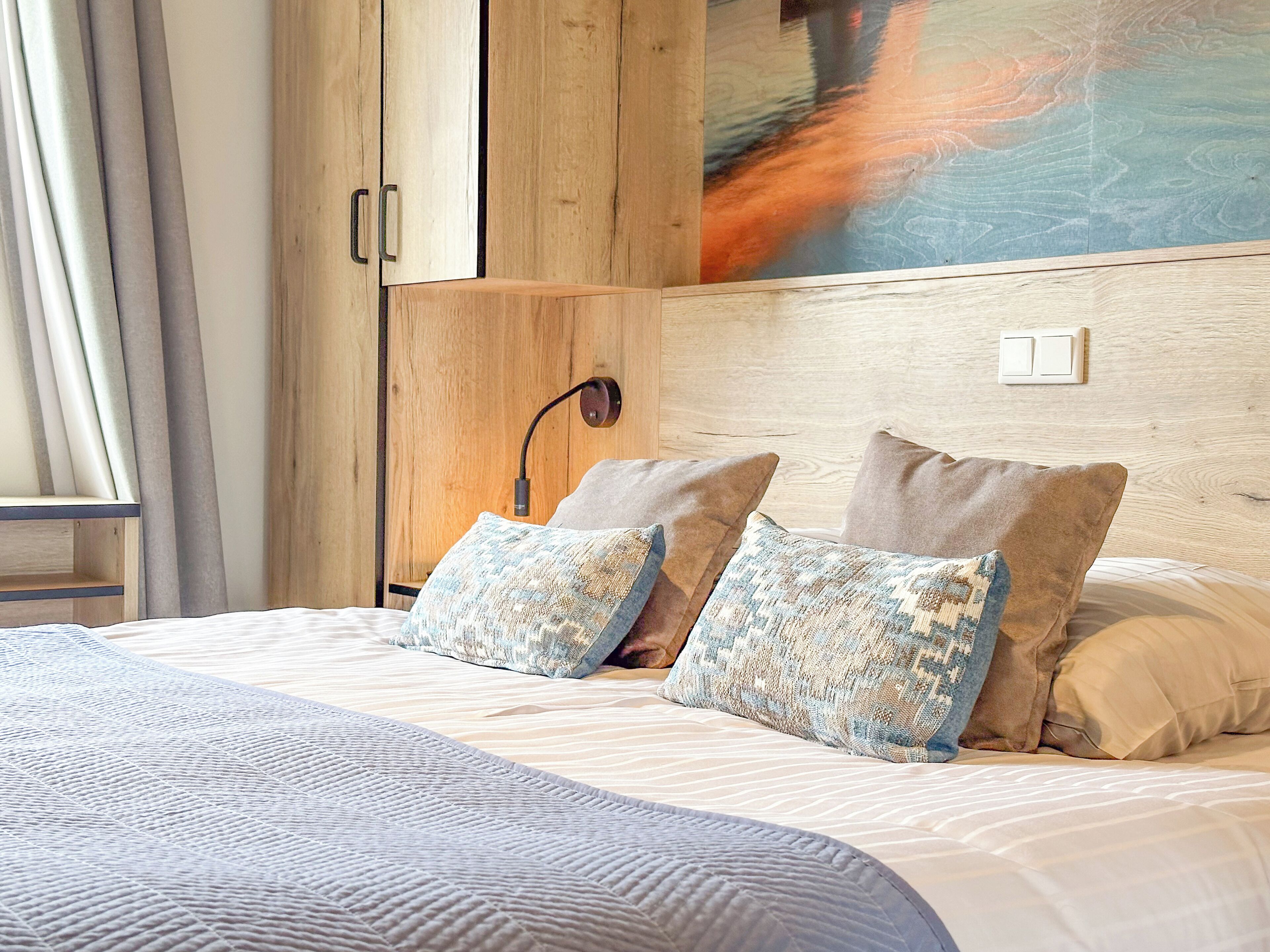 Un dormitorio con cama, almohadas, mesita de noche, lámpara y un cuadro en la pared.