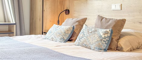 Un dormitorio con cama, almohadas, mesita de noche, lámpara y un cuadro en la pared.