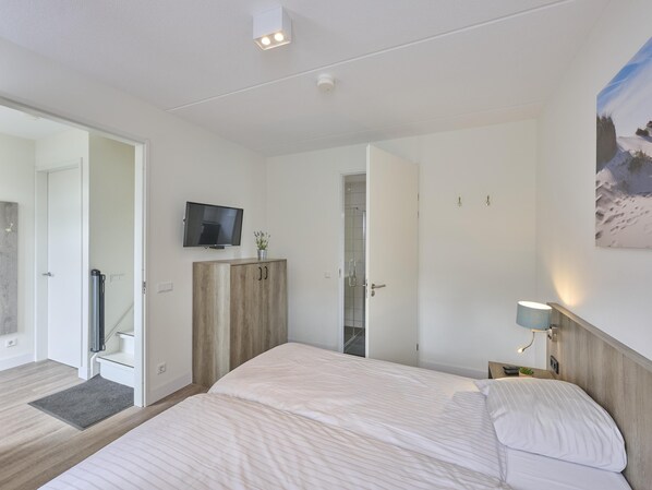 Habitación de hotel moderna con una cama grande, televisión en la pared, armario y un cuadro de un paisaje nevado.