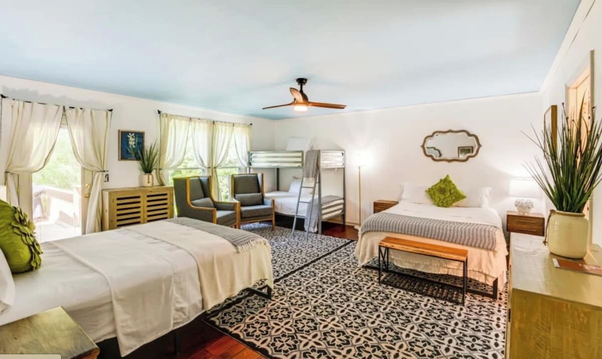 Une chambre avec deux lits, un ventilateur de plafond, un tapis à motifs et un bureau agrémenté d’une plante.