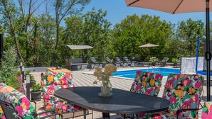 A poolside area with a round table, colorful chairs, and lounge chairs under umbrellas.