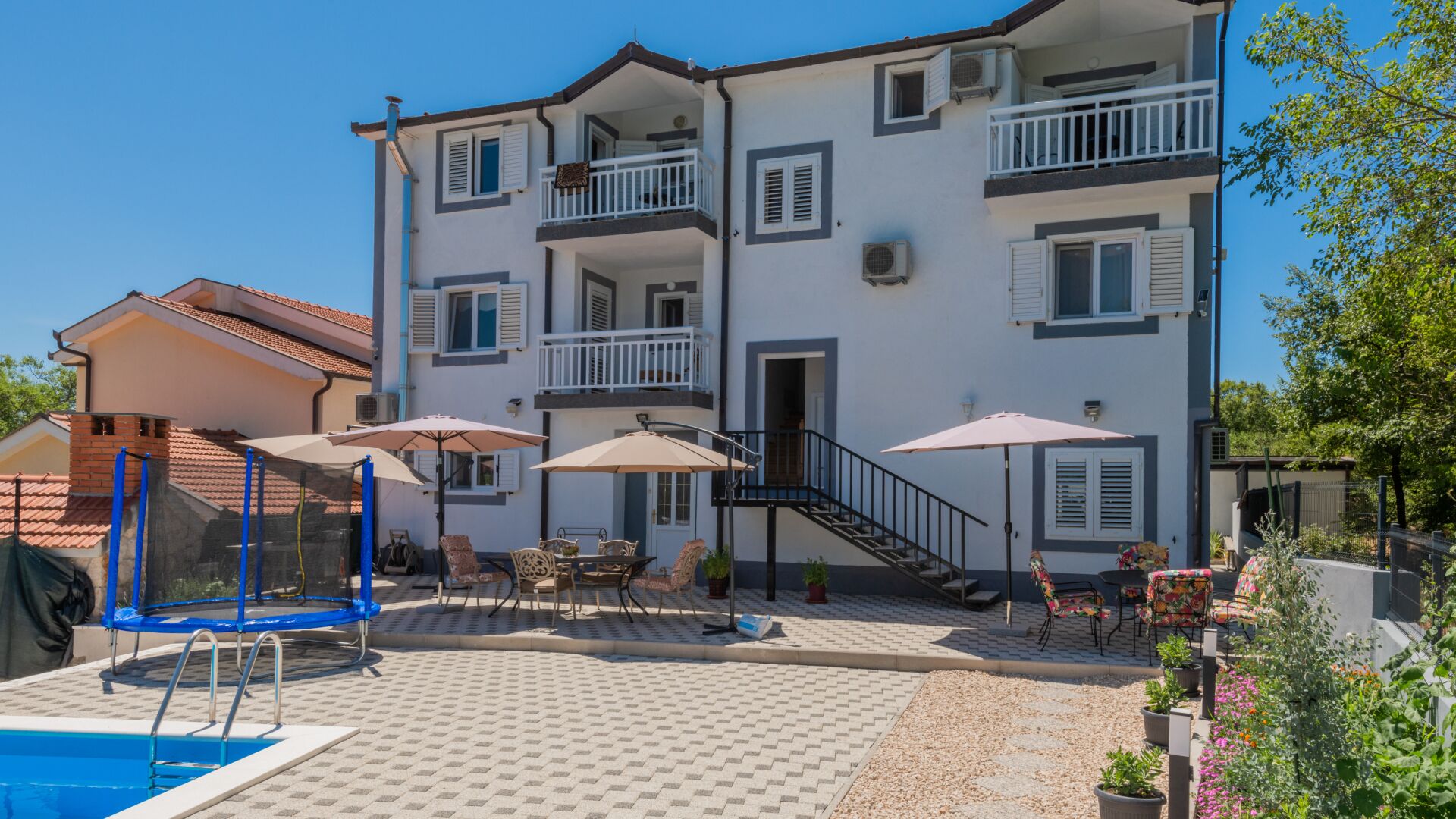 Un edificio de dos pisos con piscina, mobiliario exterior y una escalera que conduce al piso superior.