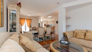 A spacious living room with a sofa set, a dining area with chairs, and a kitchen in the background.