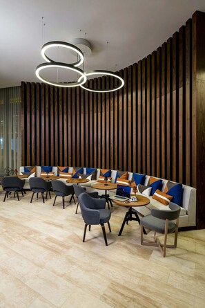 A modern lounge area with a sofa, chairs, and tables, featuring a wooden slat wall and circular ceiling lights.